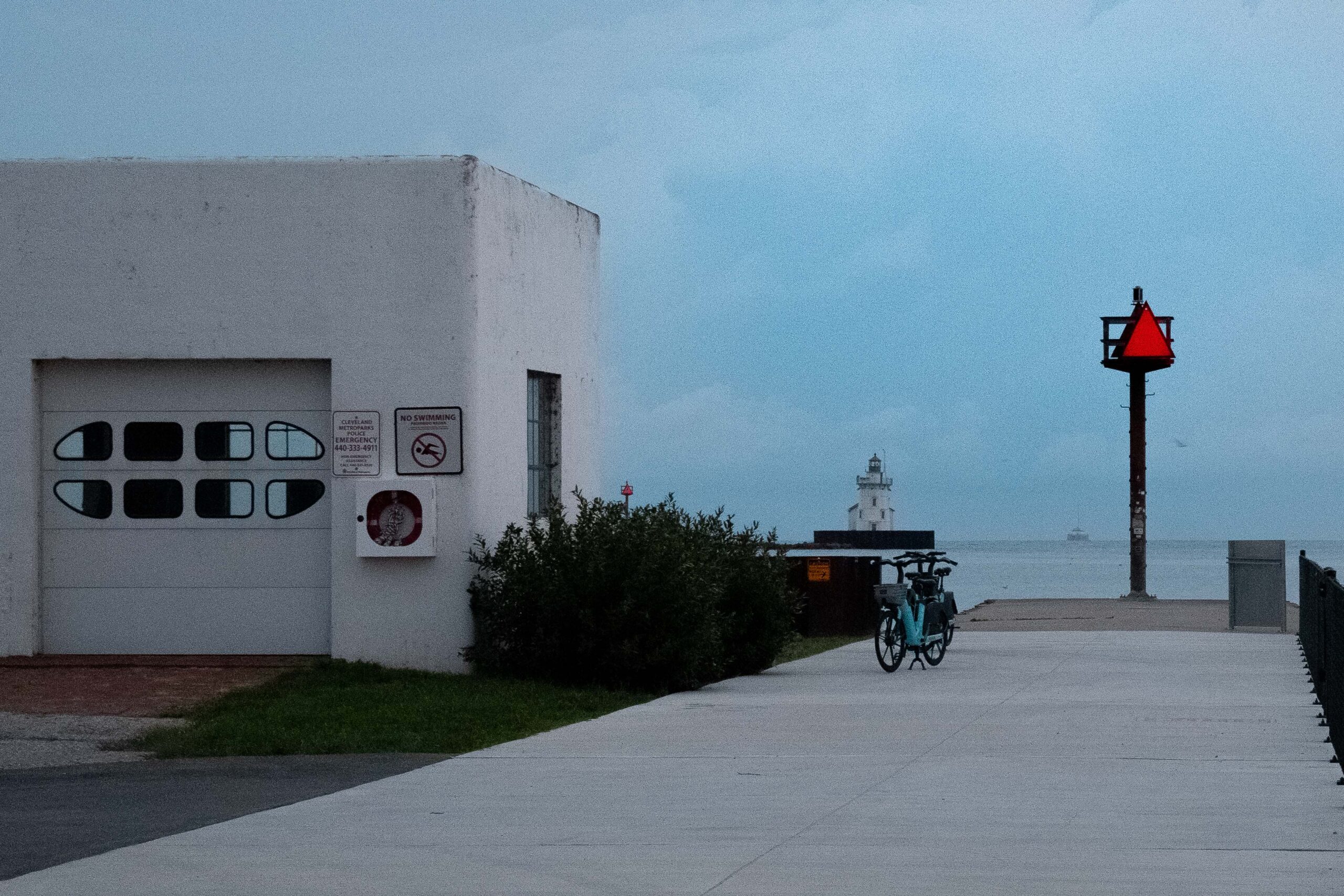 A very early morning/dark shot of the Coast Guard building at Wendy Park in Cleveland Ohio. In the foreground are a couple of rented bicycles that someone has left on the boardwalk, right in front of a lighthouse that is in the background.